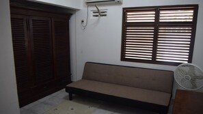 Una habitación con sofá, ventana con persianas, aire acondicionado de pared y ventilador.