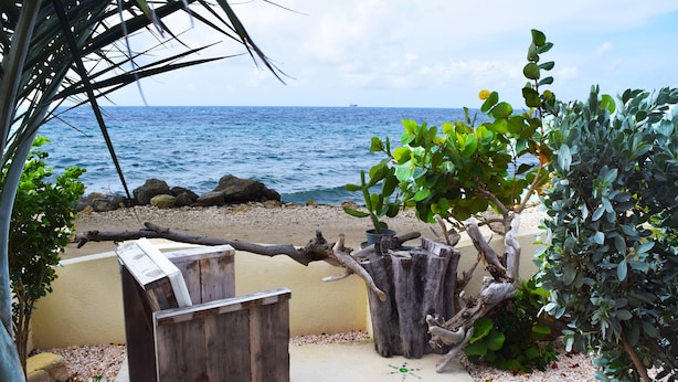A beach view with a wooden fence, a potted plant, and a rocky shoreline. - Ocean-side Home (Willemstad)