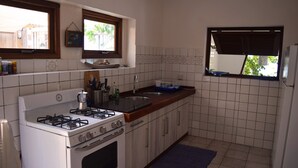 A kitchen with white cabinets, a stove, a sink, and a window with blinds. - Ocean-side Home (Willemstad)