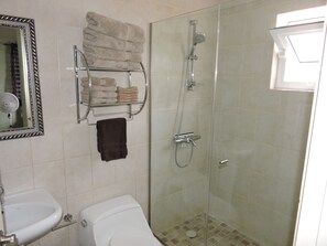 A bathroom with a glass-enclosed shower, a toilet, a sink, and a towel rack with folded towels.
