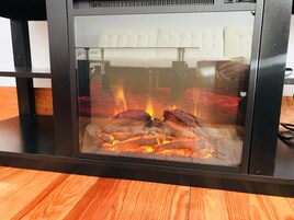 A glass-fronted fireplace with visible logs and flames, set on a wooden floor.