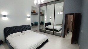 A modern bedroom with a large bed, a wardrobe with a mirror, and bedside lighting.