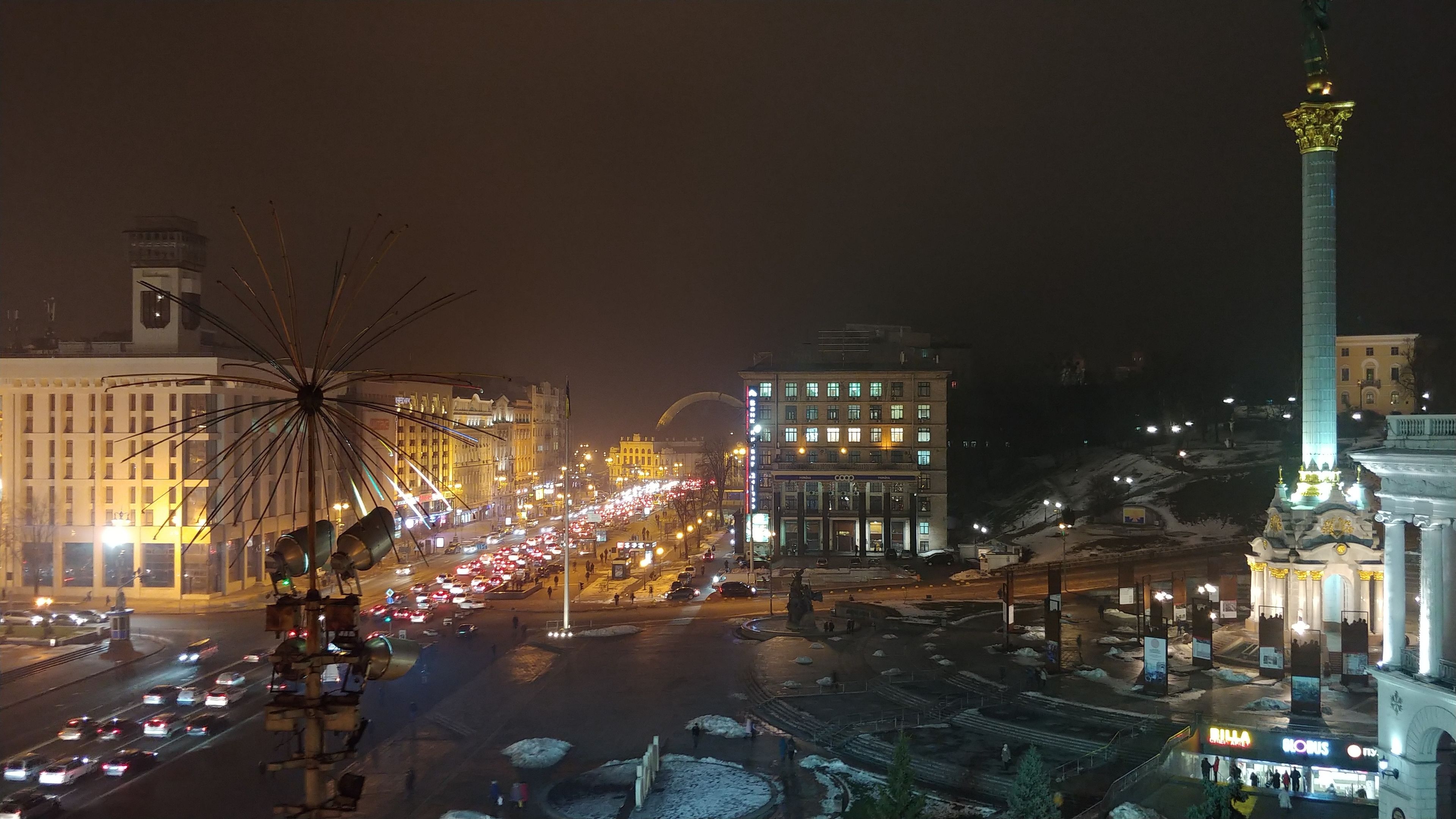 Un paisaje urbano nocturno con una noria destacada, una calle concurrida de vehículos y edificios iluminados.