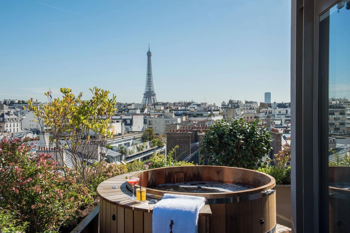 Una terraza en la azotea con un jacuzzi de madera, vista a la Torre Eiffel y un paisaje urbano de fondo.