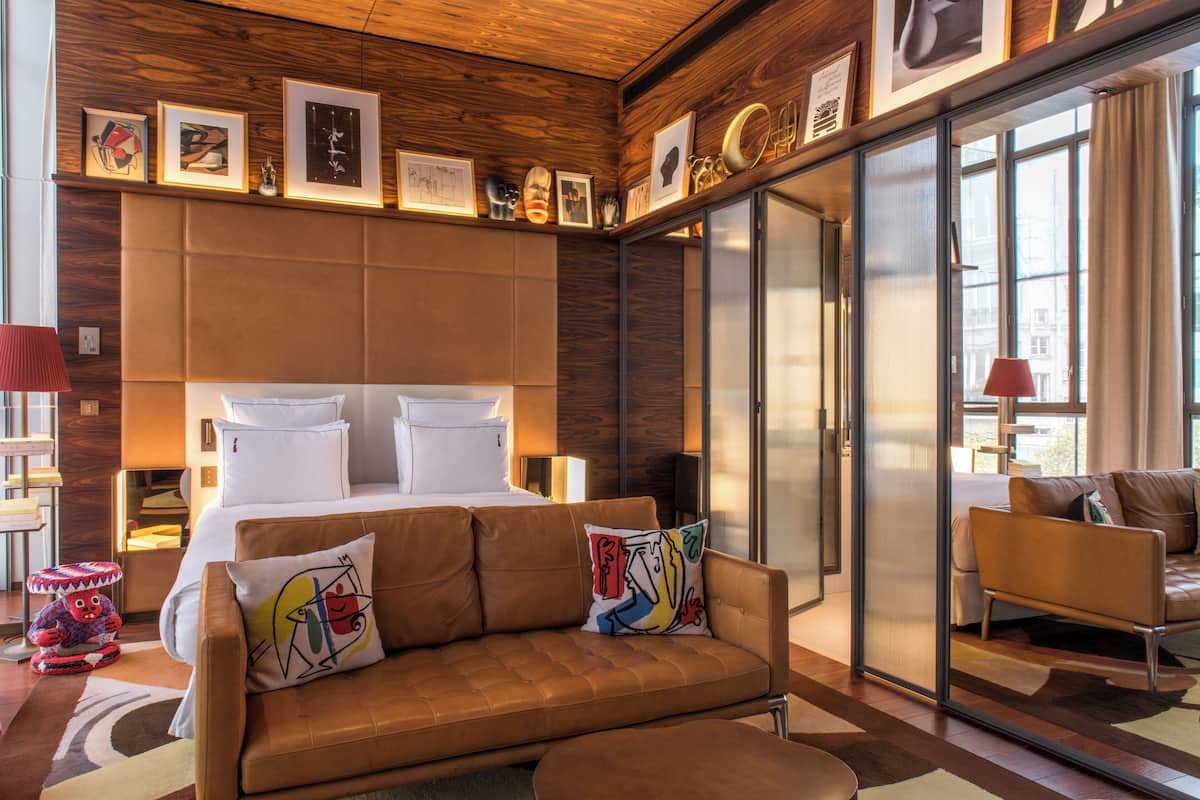Habitación de hotel moderna con una cama grande, un sofá y un ventanal de vidrio que da a un balcón.