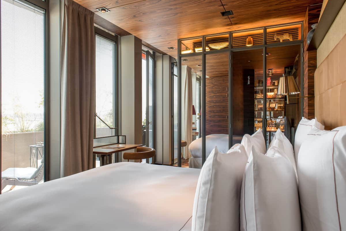 Una habitación de hotel moderna con una cama grande, una mesita pequeña, una silla y una estantería.