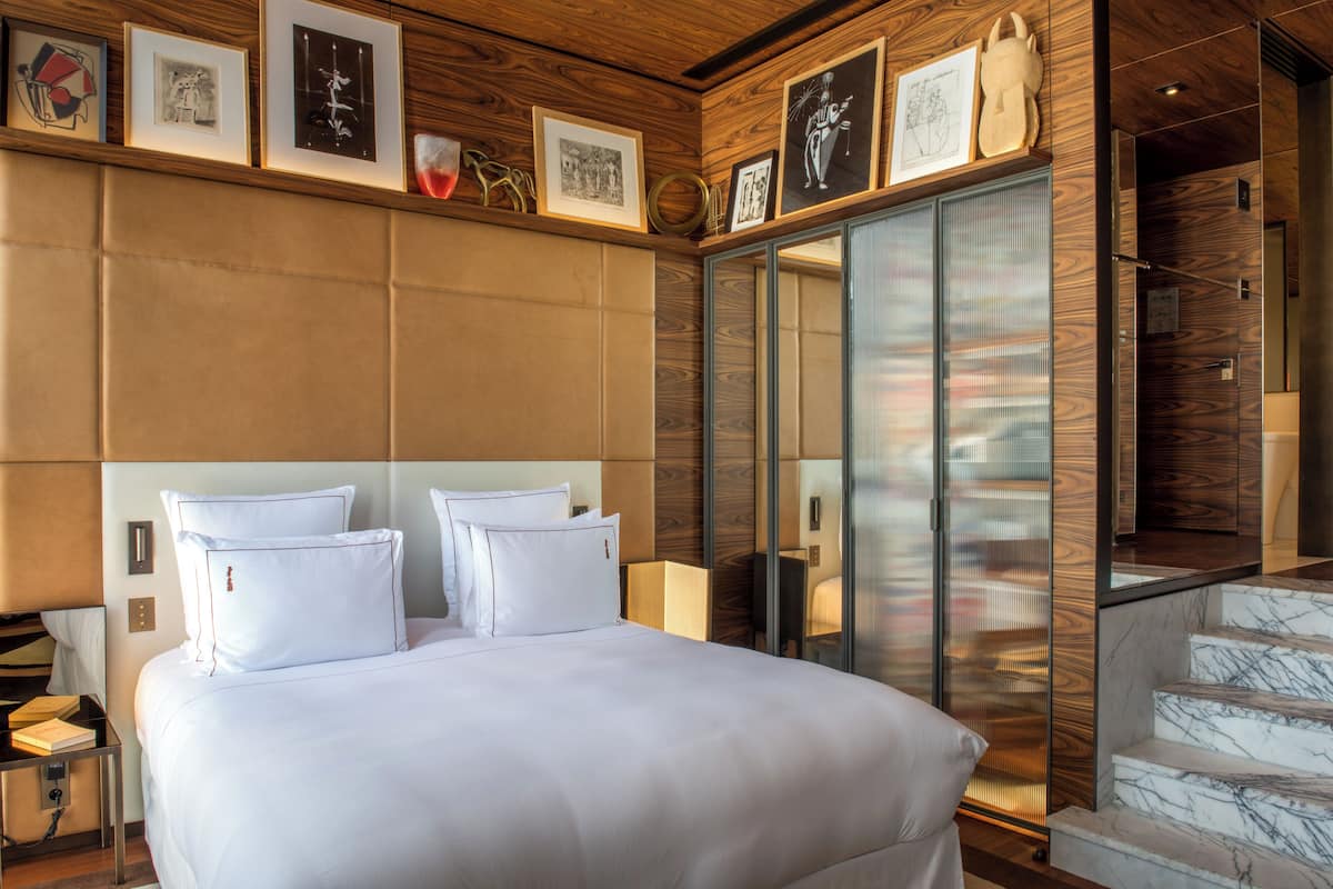 Una habitación de hotel moderna con una cama grande, cabecera de madera y puerta de cristal que da a un balcón.