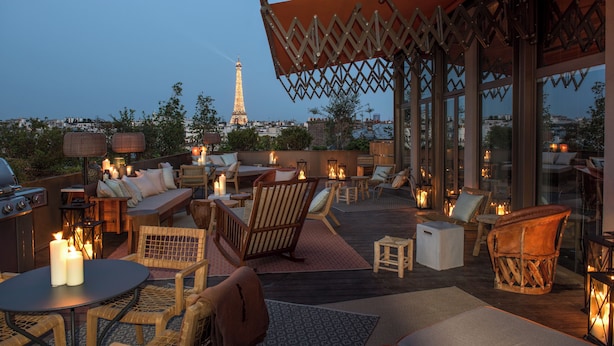 An outdoor seating area with wicker furniture, candles, and a view of the Eiffel Tower. - Brach Paris - Evok Collection (Paris)