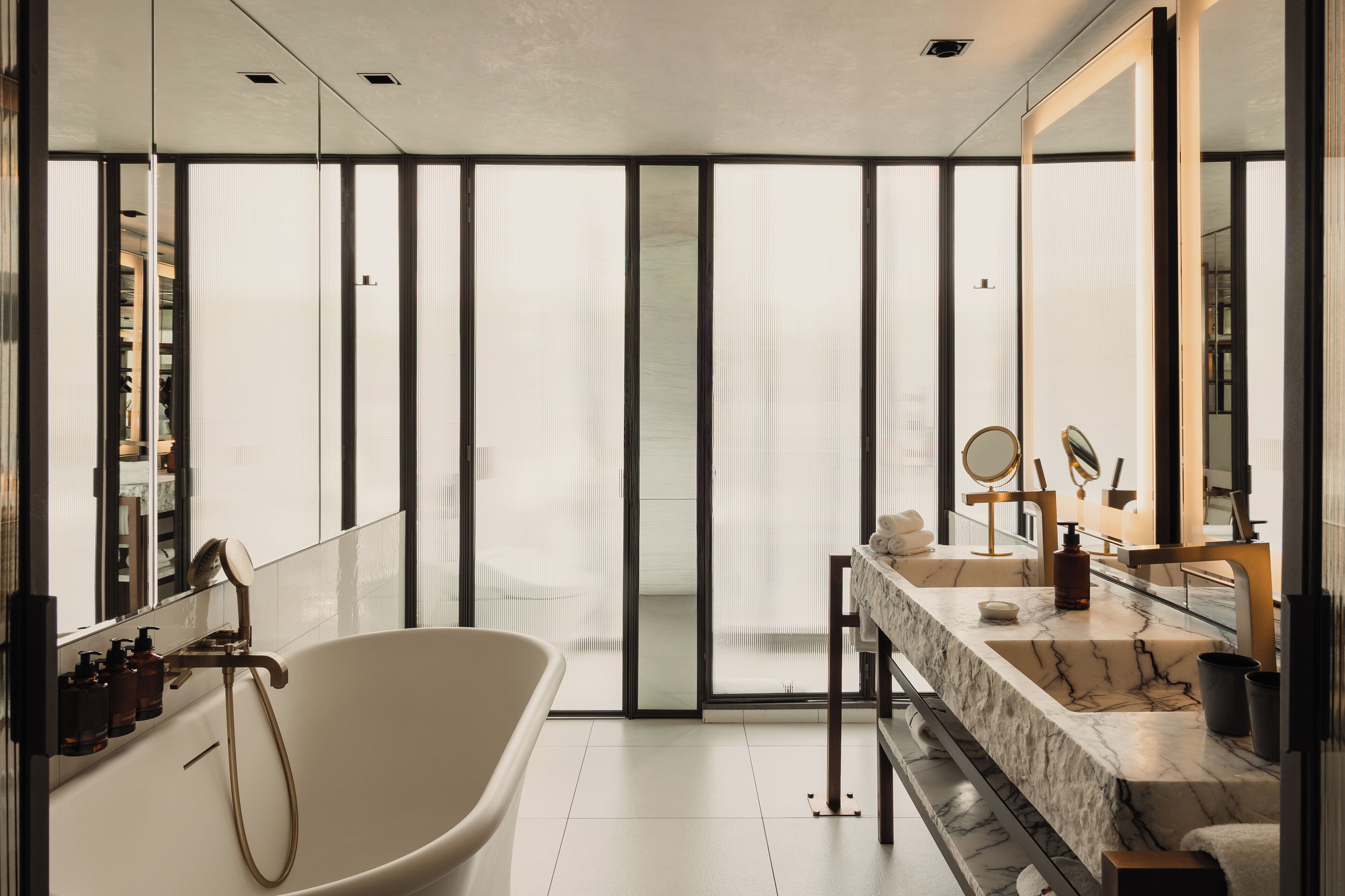 A modern bathroom with a freestanding bathtub, a large mirror, and a vanity with a marble countertop.