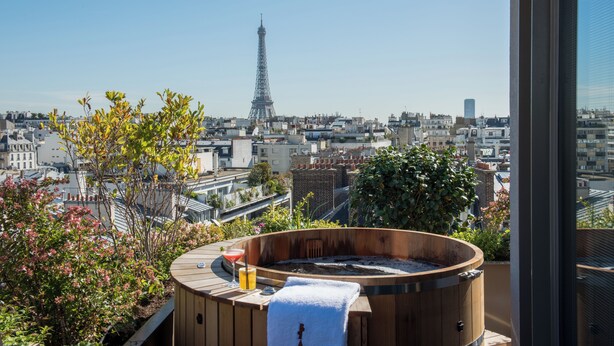 A hot tub with a towel and a drink on a balcony overlooking the Eiffel Tower.
