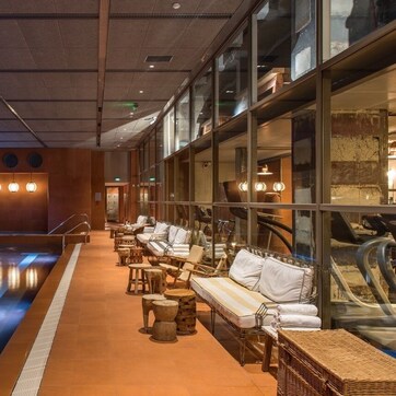 A spa area with a pool, lounge chairs, and a glass wall.