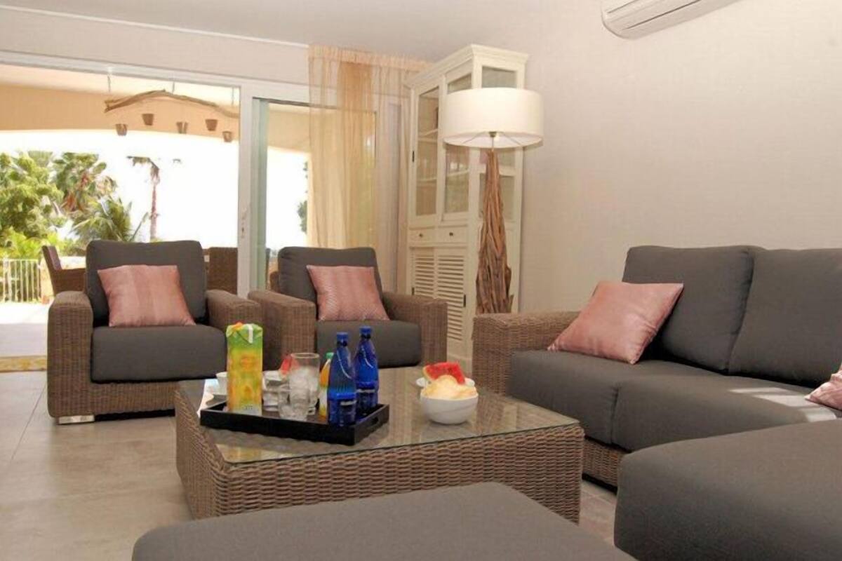 A living room with two sofas, a coffee table with drinks, and a large window with curtains.