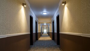 A long, narrow hallway with patterned walls and carpet, leading to a bright end. - Hotel Stil (Cluj-Napoca)