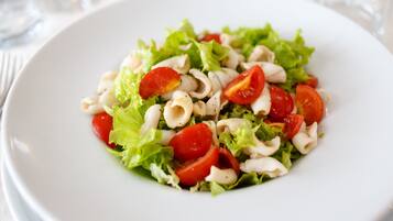 A white plate with a salad consisting of lettuce, cherry tomatoes, and pasta.