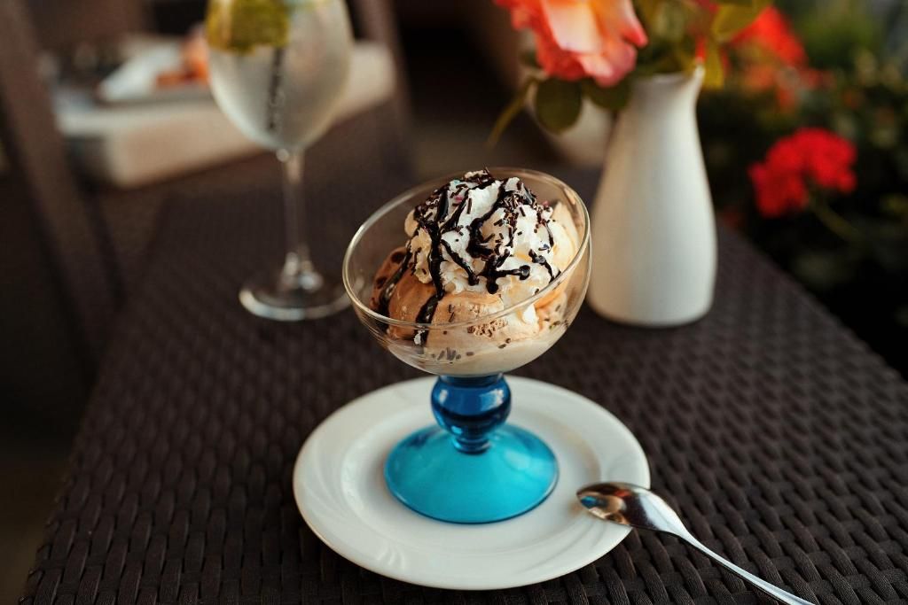 A dessert in a clear glass bowl on a white plate with a blue base, accompanied by a spoon.