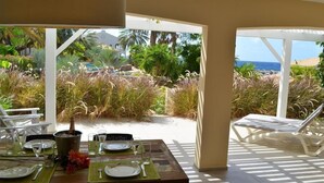 Un espace de restauration en plein air avec une table dressée pour deux personnes, entouré d’une végétation tropicale luxuriante et offrant une vue sur la plage.