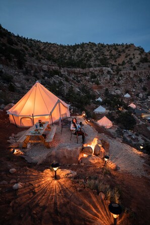A tented accommodation with a picnic table and a fire pit, surrounded by rocky terrain and other tents. - Zion Glamping Adventures (Hildale)