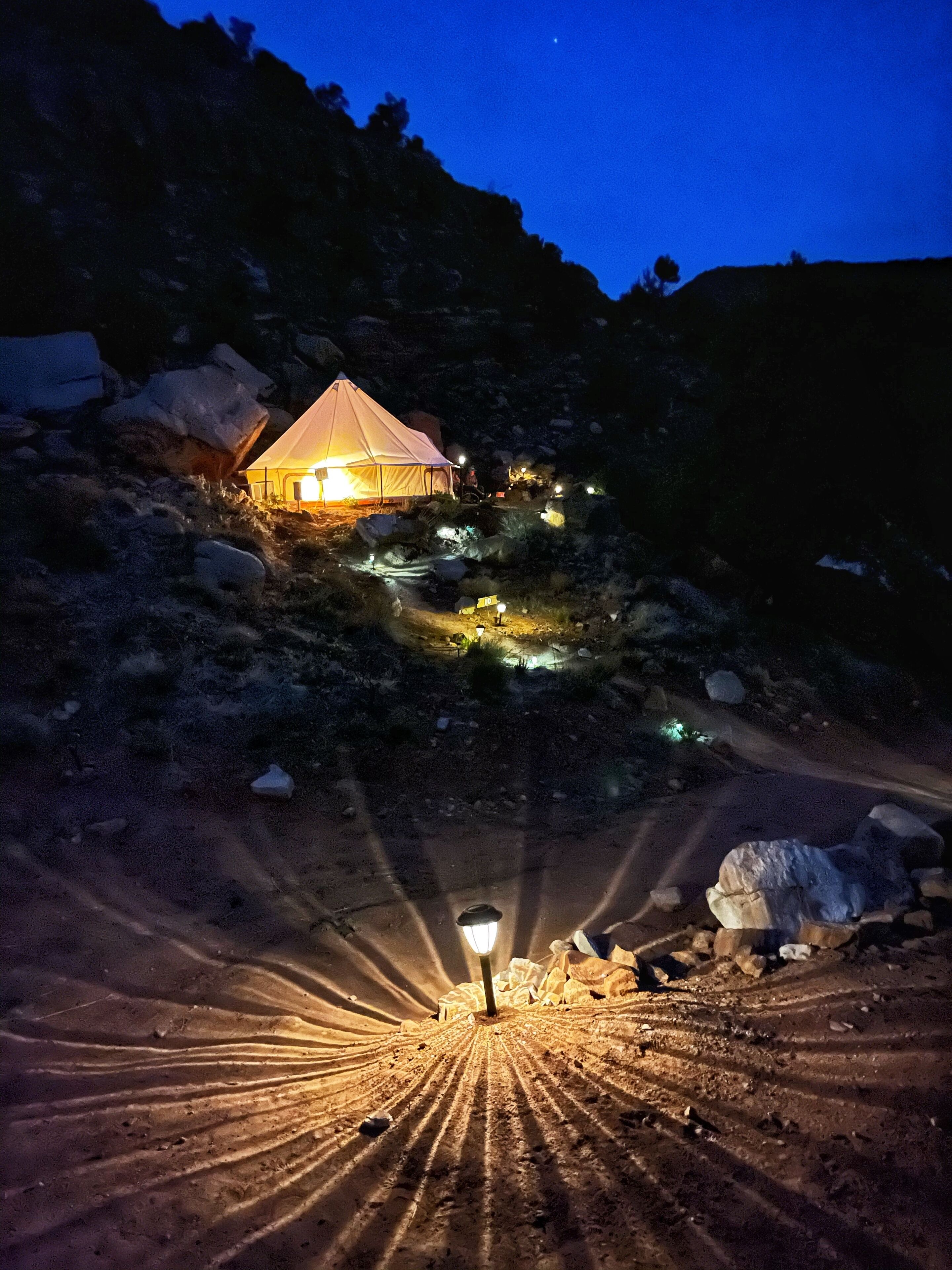 A tented accommodation with a single room, surrounded by rocky terrain and sparse vegetation.