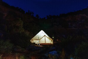 Acomodação em tenda com teto inclinado, rodeada por paisagem natural sob um céu estrelado.