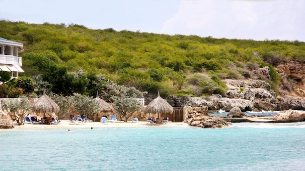 A beach with thatched-roof huts, lounge chairs, and a rocky shoreline. - Ocean Resort Villa Condor (Willemstad)