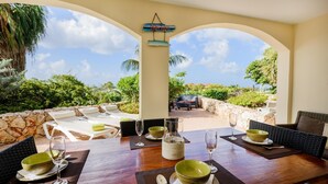 A dining area with a view of a stone wall and greenery, a sign reading "RONDAD", and outdoor seating with a stone wall backdrop. - Ocean Resort Villa Condor (Willemstad)