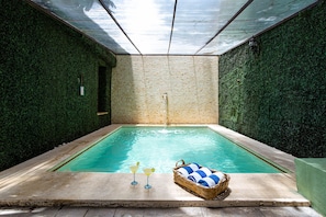 An indoor swimming pool with a brick wall, a waterfall feature, and a wicker basket with towels. - Viva Merida Hotel Boutique (Mérida)
