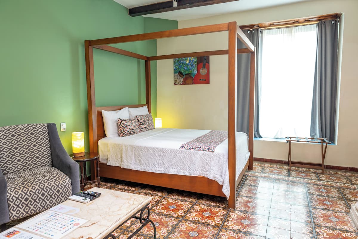 A four-poster bed with a wooden frame, a patterned sofa, a small table with a lamp, and a window with curtains.