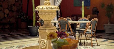 Un coin repas avec une table dressée pour deux personnes, une fontaine décorative et diverses plantes.
