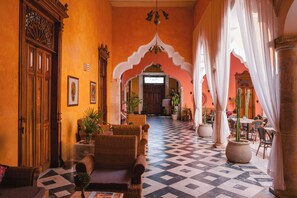 A hotel lobby with a checkered floor, wicker furniture, and a large wooden door. - Viva Merida Hotel Boutique (Mérida)