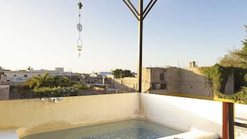Una terraza en la azotea con jacuzzi, mobiliario exterior y vistas panorámicas de la ciudad.