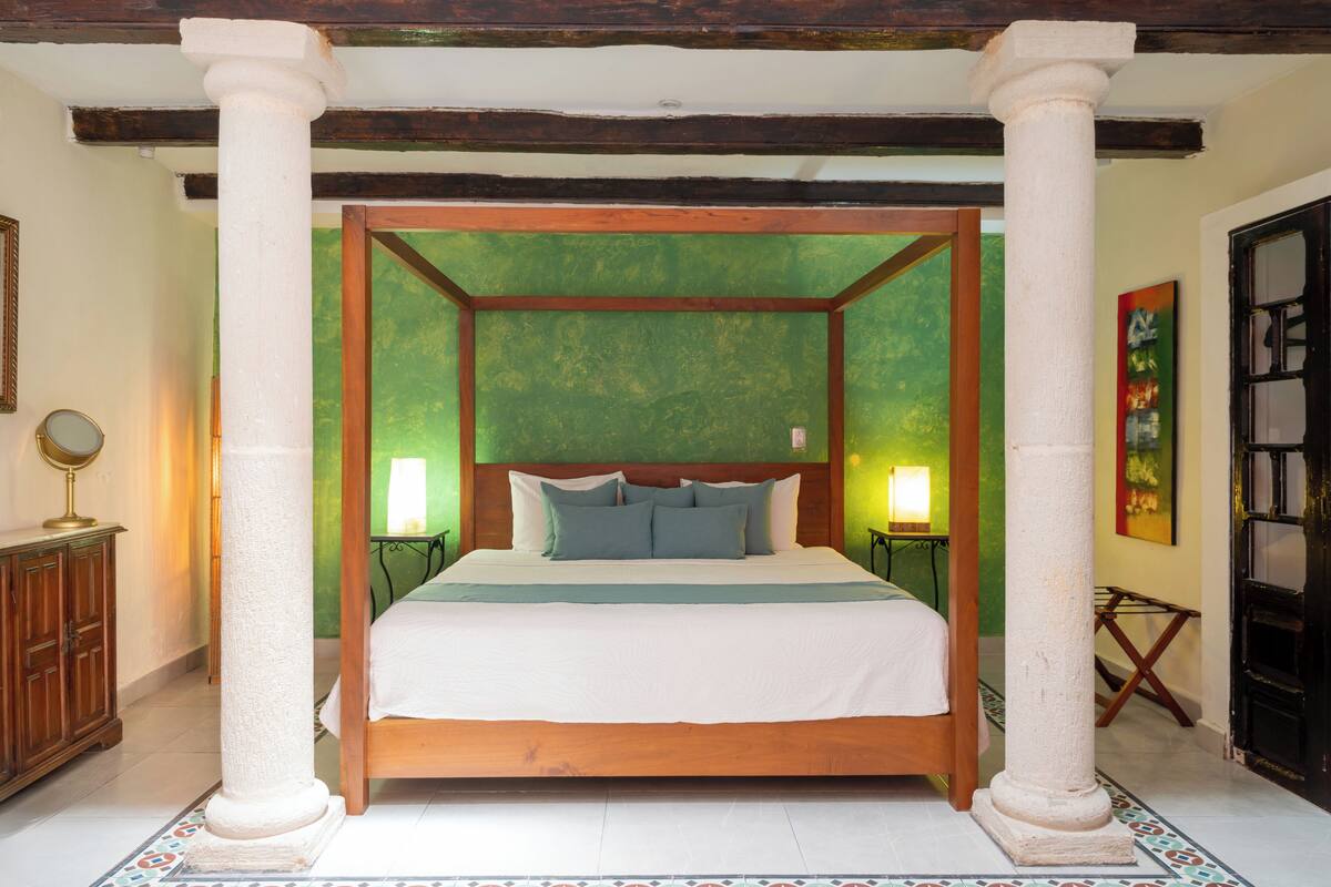 A four-poster bed with a wooden frame and white columns, a green wall, and two bedside lamps.