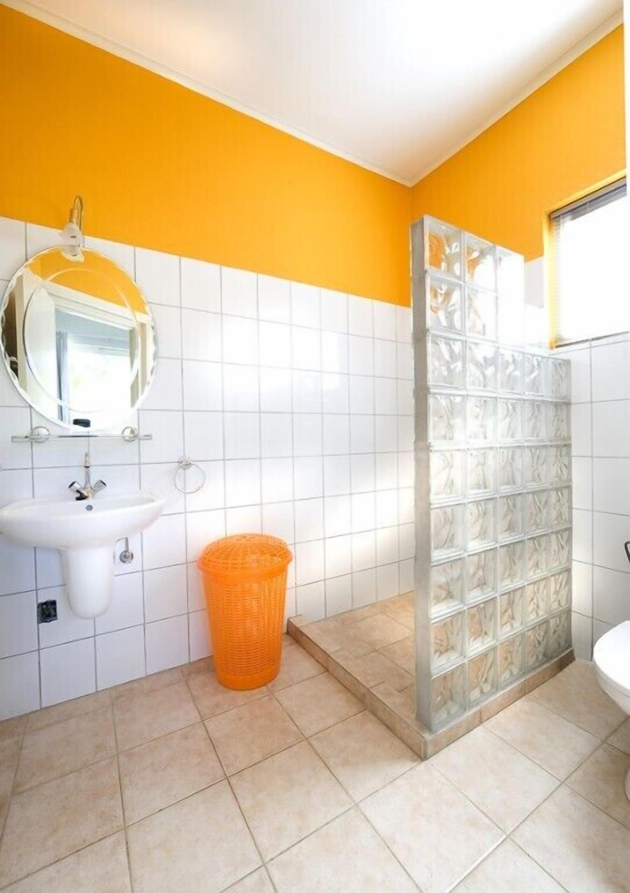 A bathroom with a white sink, mirror, and toilet. There is a glass shower enclosure and a trash bin.