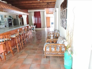 A spacious kitchen with a long counter and bar seating, wooden chairs, and a wicker sofa. - Luxurious Villa with Great Sea View (Sabana Westpunt)