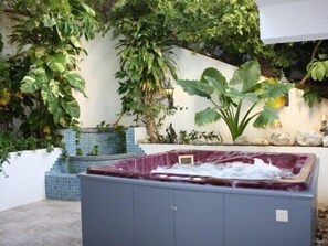 A spa area with a hot tub, surrounded by lush greenery and a tiled wall.