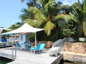 A dock with lounge chairs and umbrellas, a boat with 'NC' on it, and lush greenery. - Luxury 3 bedroom Villa at Water's Edge (Willemstad)