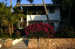 A two-story house with a stone wall and a staircase leading to the entrance.