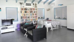 Ein Wohnzimmer mit Bücherregal, Fernseher, Essbereich und Deckenventilator.