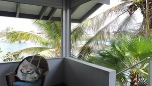 Ein Blick auf Pool und Palmen von einem Zimmer aus, ein Korbsessel mit einer Tasche und ein Metallgeländer.