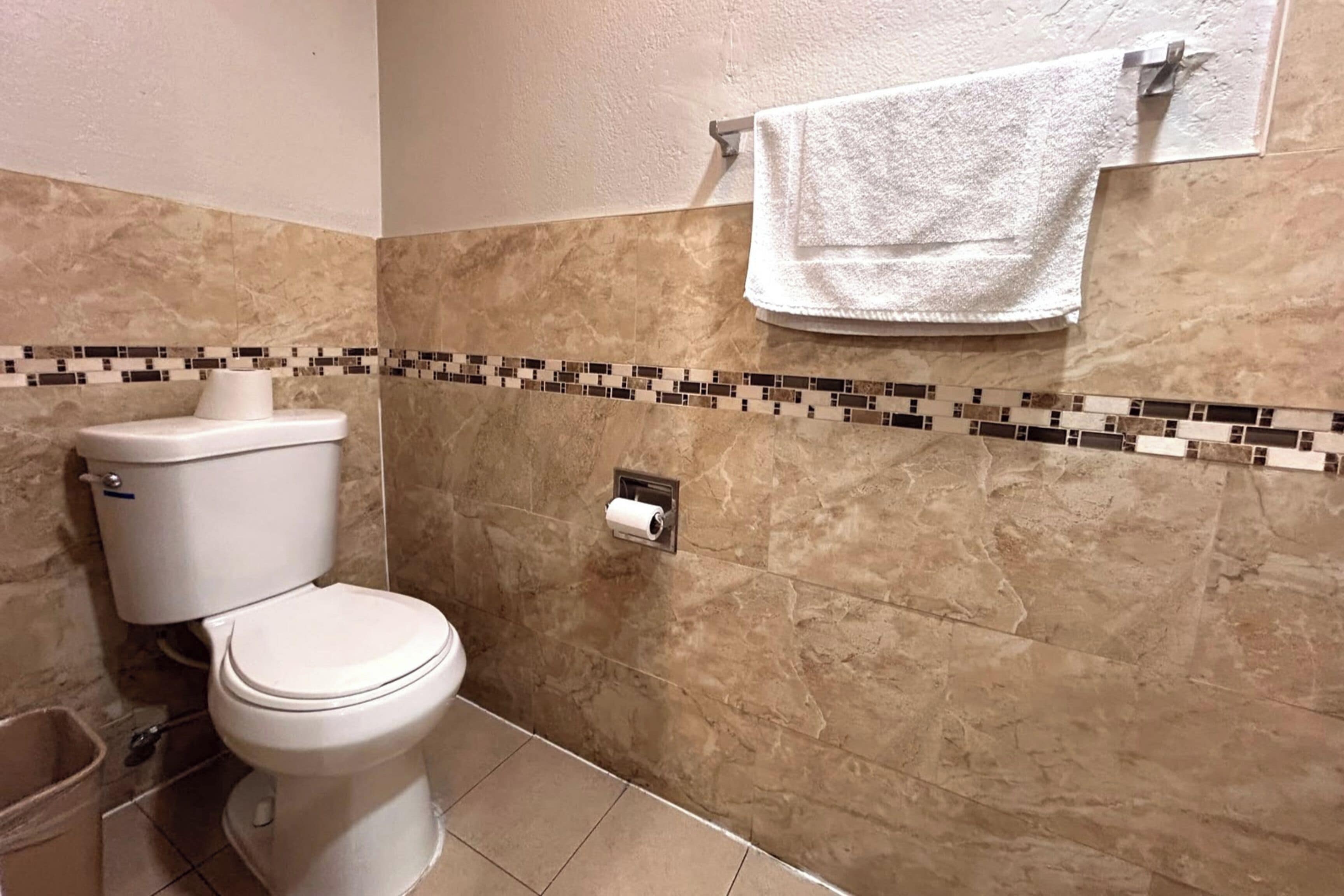 Un baño con inodoro, toallero con toalla y soporte para papel higiénico.