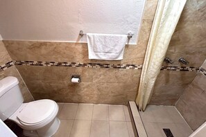 Een compacte badkamer met tegels, een toilet, een douche en een handdoekhouder.