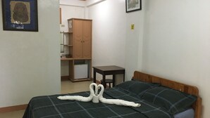 Een kamer met een bed, een houten garderobe, een klein tafeltje en een fotolijst aan de muur.