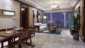 Una habitación de hotel moderna con comedor, sofá, mesa de centro y un ventanal con vistas a la ciudad.