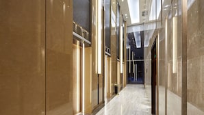 Un pasillo moderno y bien iluminado, con pisos y paredes reflectantes, que conduce a una puerta de cristal al final.