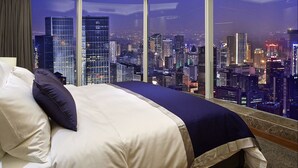 Habitación de hotel con techo curvo, cama grande con ropa blanca, almohadas azul oscuro y vista a la ciudad de noche.