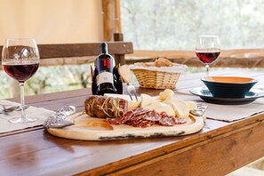 A wooden table with a cheese board, sliced meats, a bottle of wine, and glasses of red wine.