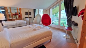 Habitación de hotel con cama, una silla roja, televisión y ventana con vistas a zonas verdes.