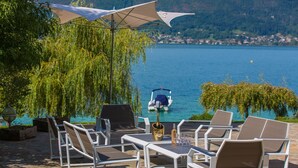 Un espacio al aire libre con sillas y una mesa, con vistas a un lago y un barco al fondo.