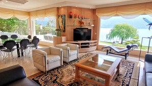 Una sala de estar moderna con televisor, asientos y vistas a un lago.