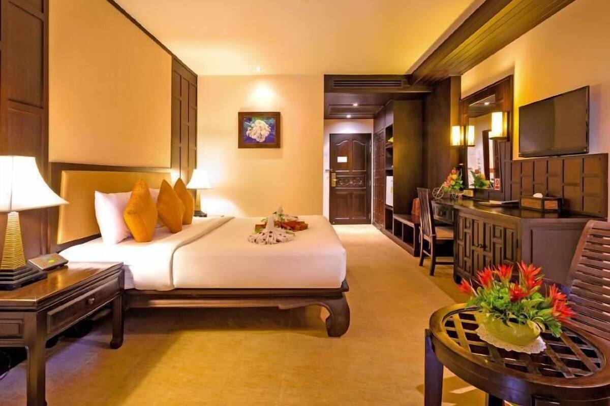 Une chambre d’hôtel avec un lit, une table de chevet, une lampe et une petite table agrémentée d’un arrangement floral.
