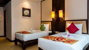 A hotel room with two beds, each with a pillow and a small table. There is a painting on the wall and a lamp on the nightstand. - Nipa Resort (Phuket)